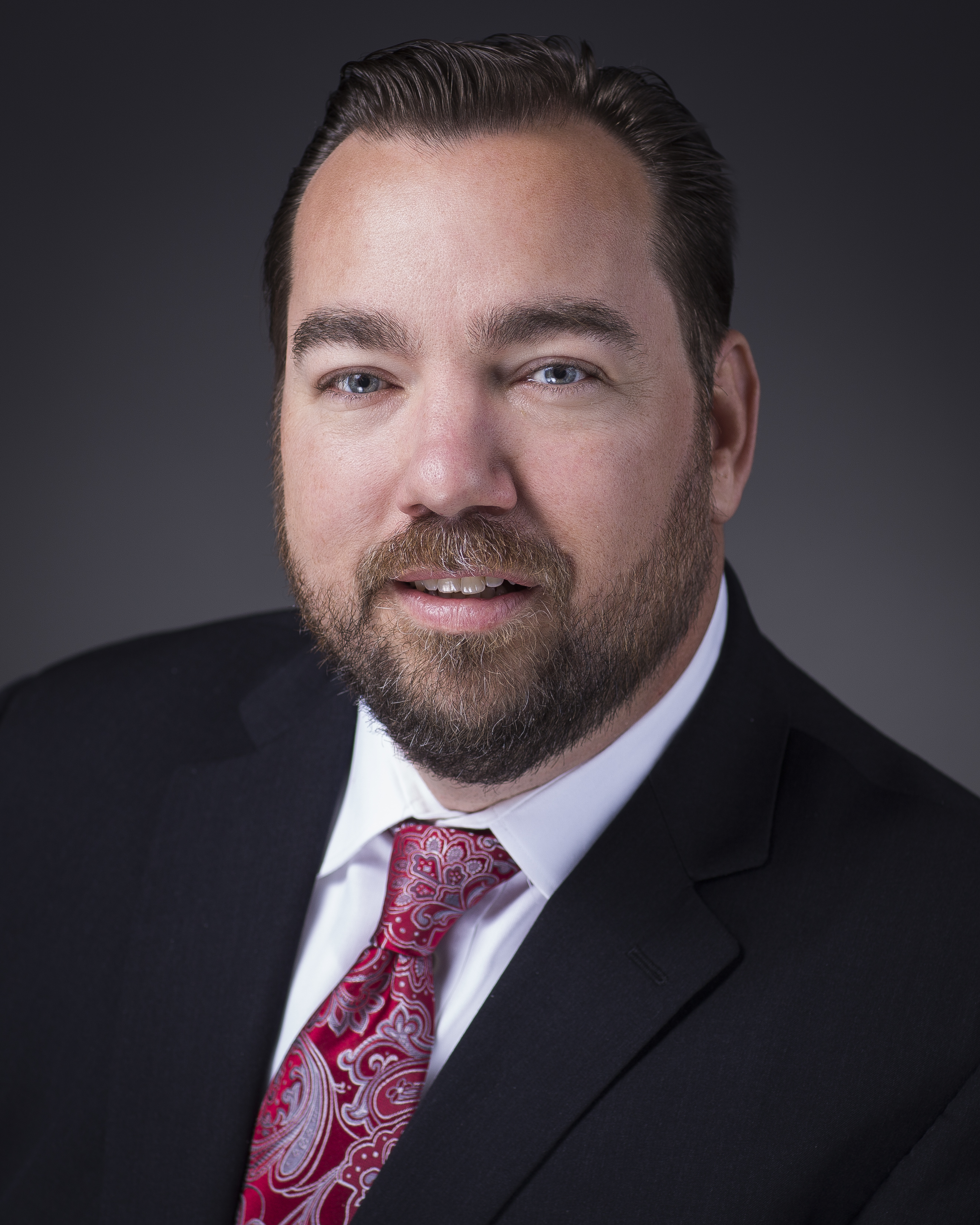 A person wearing a suit and tie smiling at the camera    Description generated with very high confidence